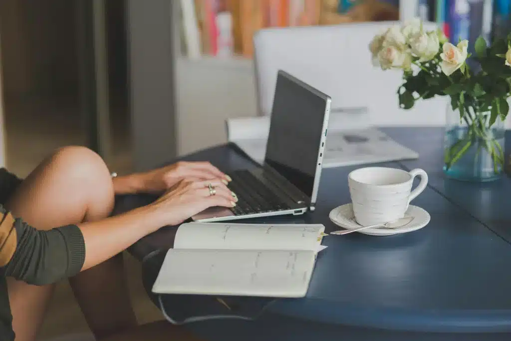 A person sits at a desk typing on a laptop with a notebook open and a cup of coffee nearby. This cozy study setup is perfect for exploring bar exam study resources in a calm, focused space.